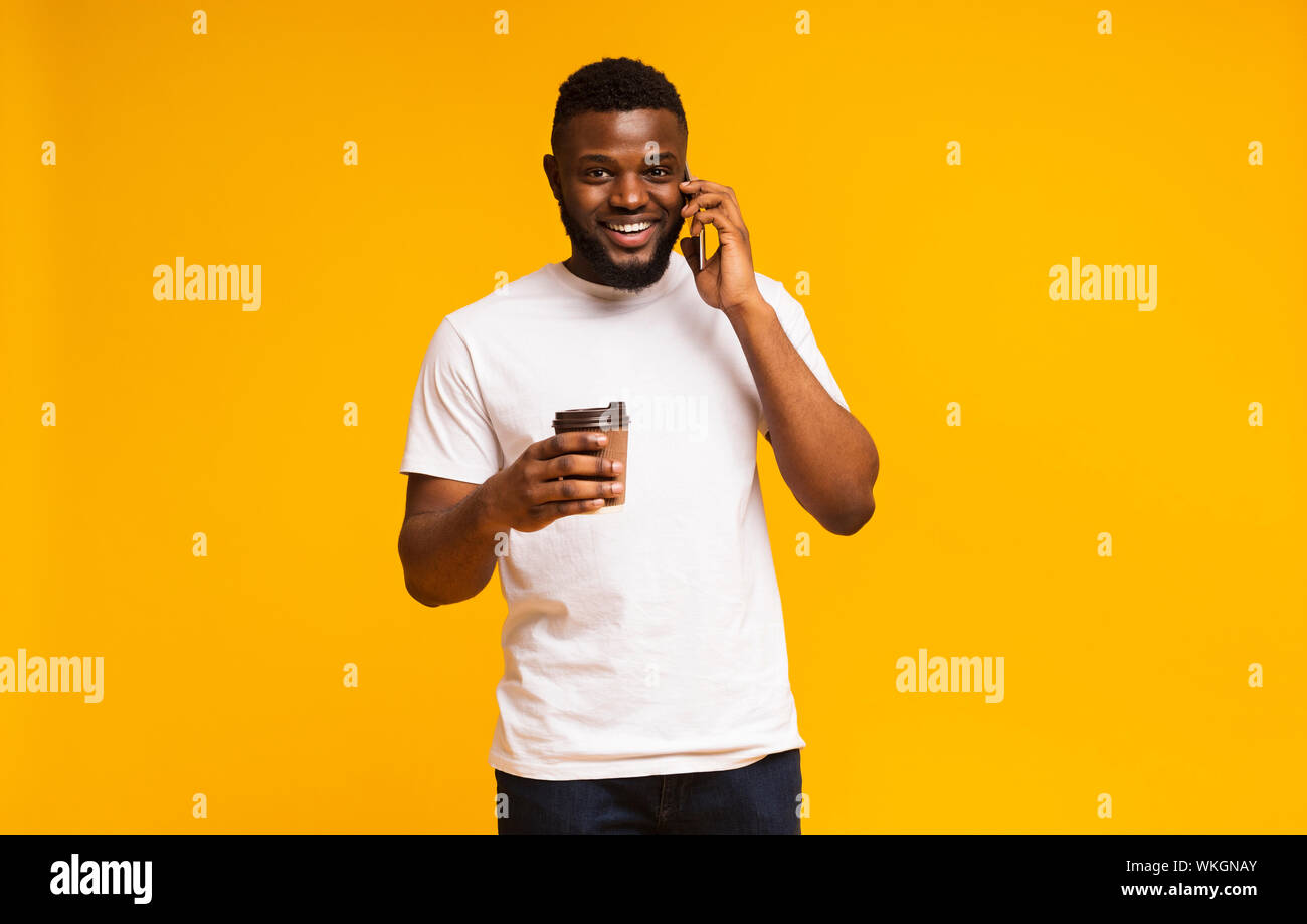 Young man holding cup of coffee and talking on smartphone Stock Photo