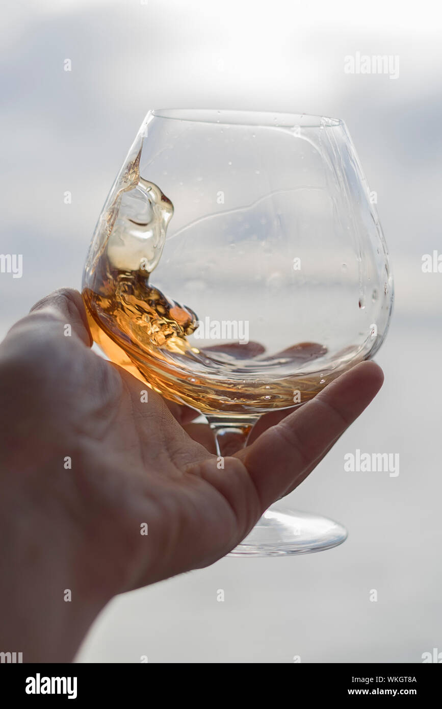 Cropped Image Of Hand Holding Brandy Snifter Against Sea Stock Photo