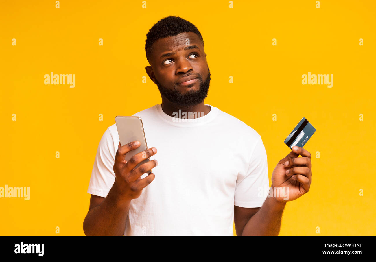 Doubtful african guy holding cellphone and credit card Stock Photo