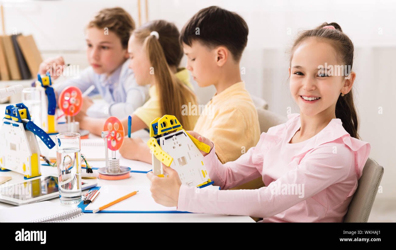 Happy schoolgirl holding robot model in classroom Stock Photo