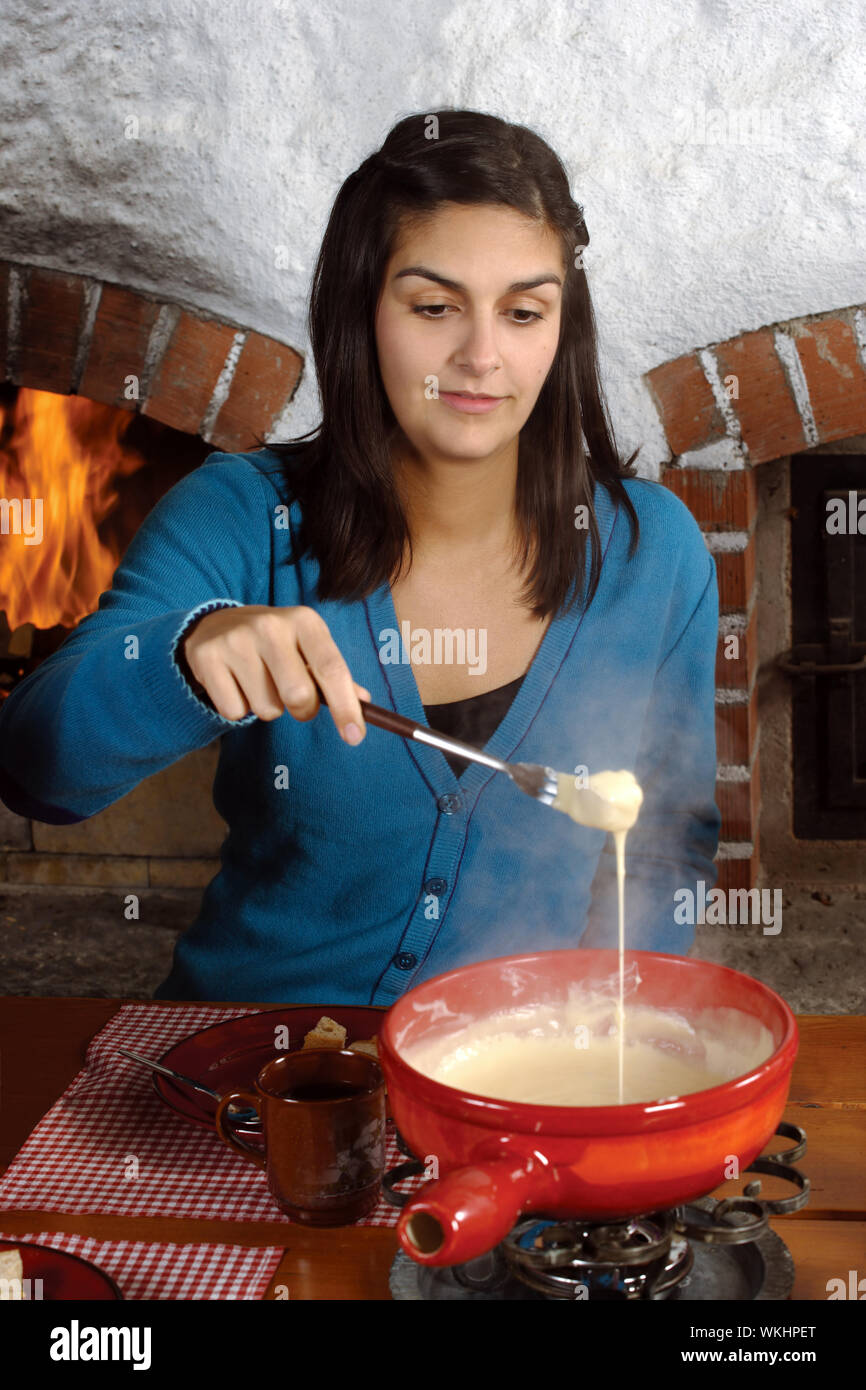 Photo of a beautiful female dipping bread into the melted cheese in a