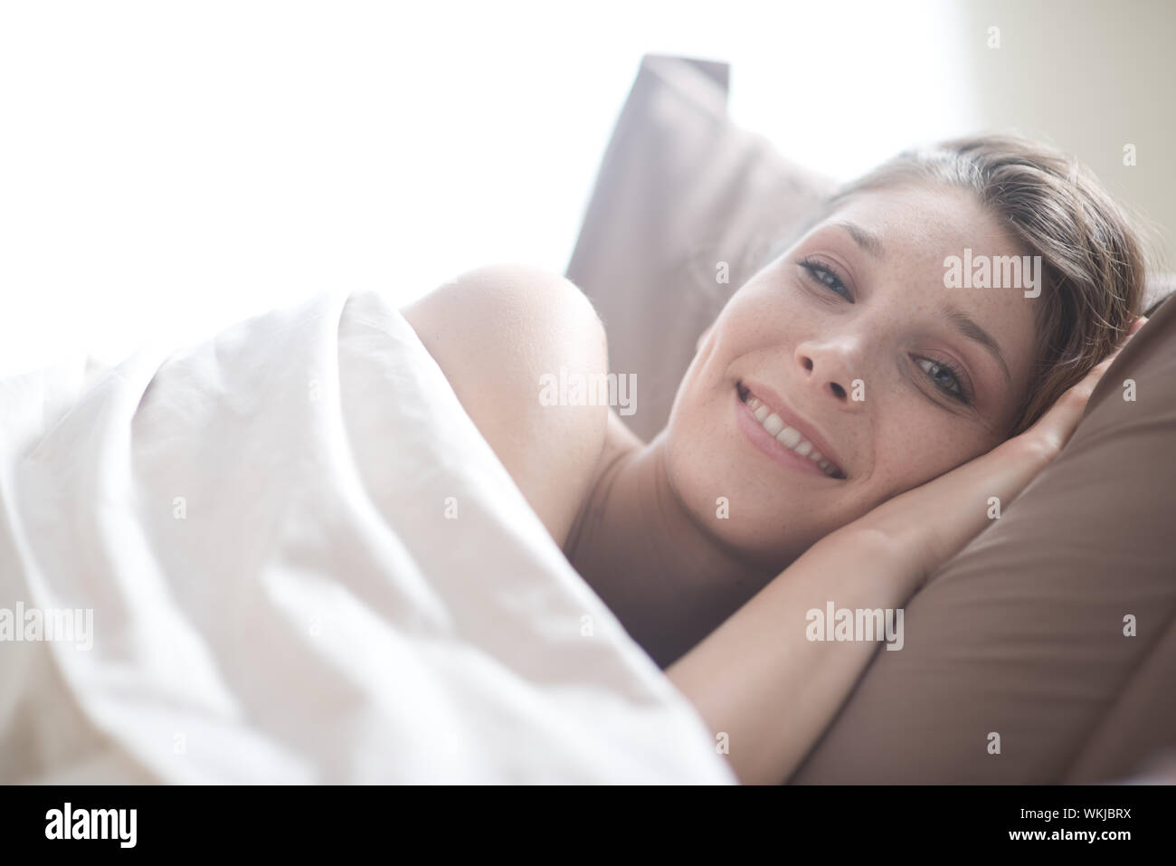 Young woman lying in bed and smiling at the camera Stock Photo - Alamy