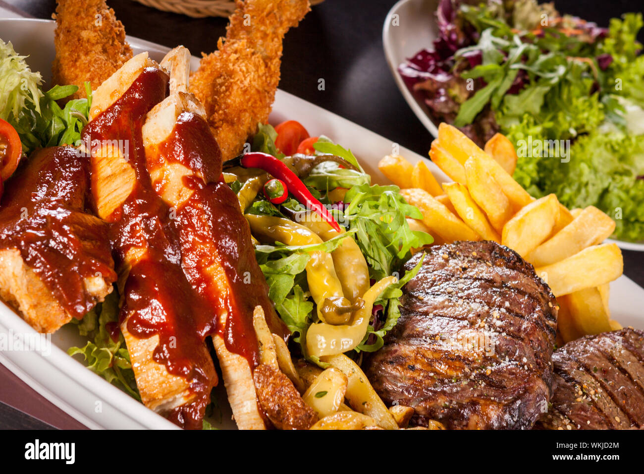 Wholesome platter of mixed meats including grilled steak, crispy crumbed chicken and beef on a bed of fresh leafy green mixed salad served with French Stock Photo