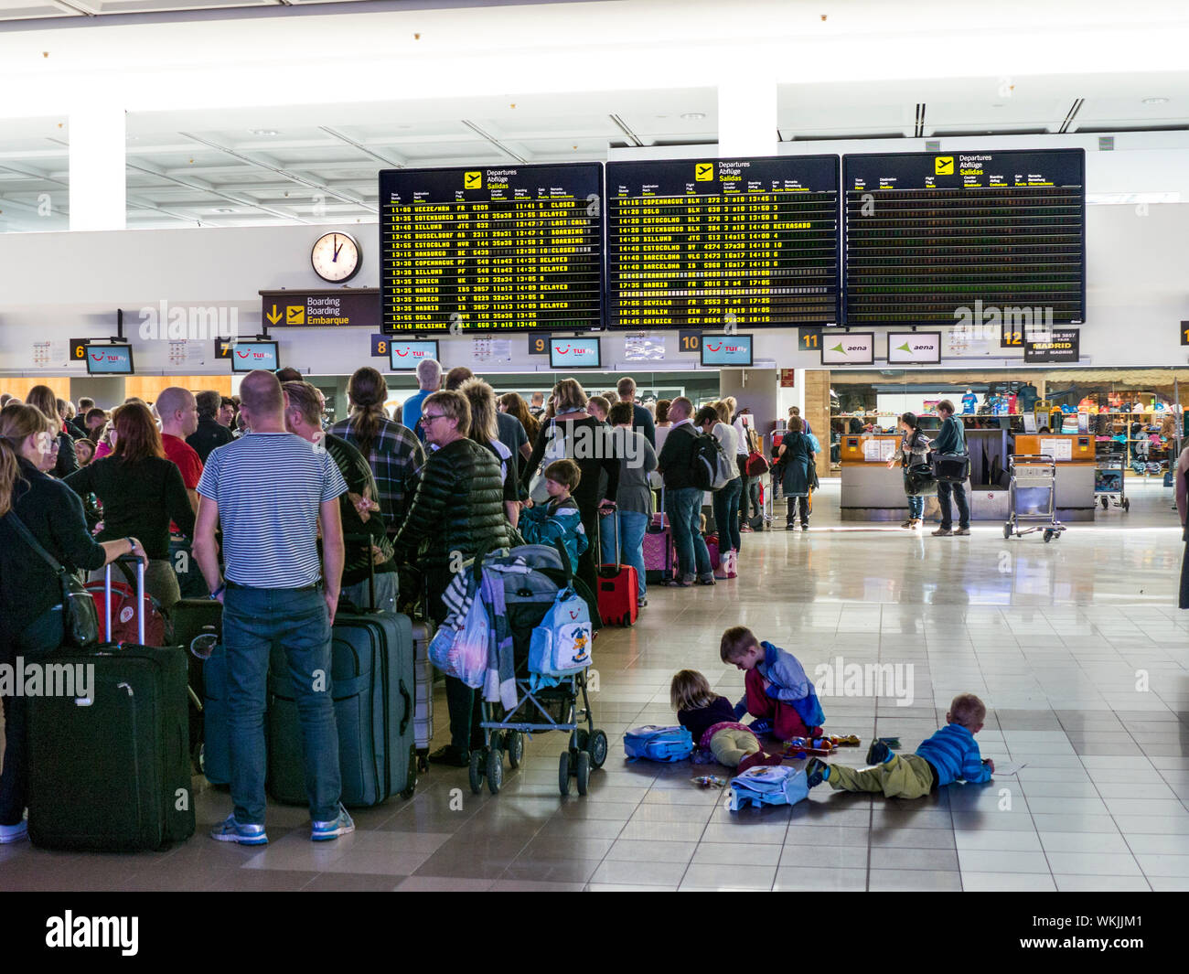 AIRPORT TUI CHECK-IN QUEUE QUEUES PASSENGERS BORED CHILDREN HOLIDAY FLIGHT DELAYS INFORMATION SCREENS QUEUES Delayed passenger queues of holiday charter flight passengers and luggage wait at airport terminal to check in baggage to their flight Spain Stock Photo