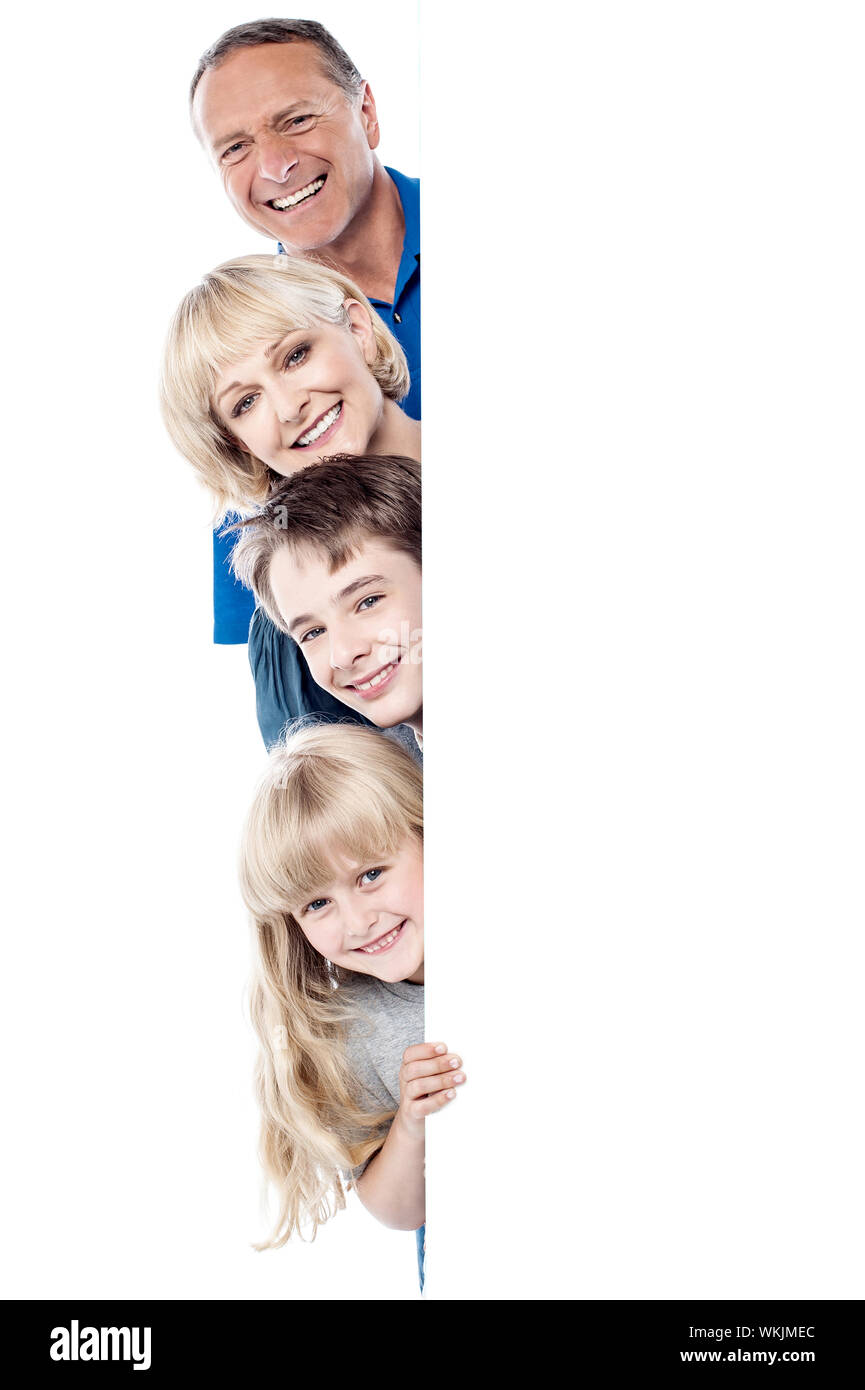 Smiling family posing from behind blank whiteboard Stock Photo