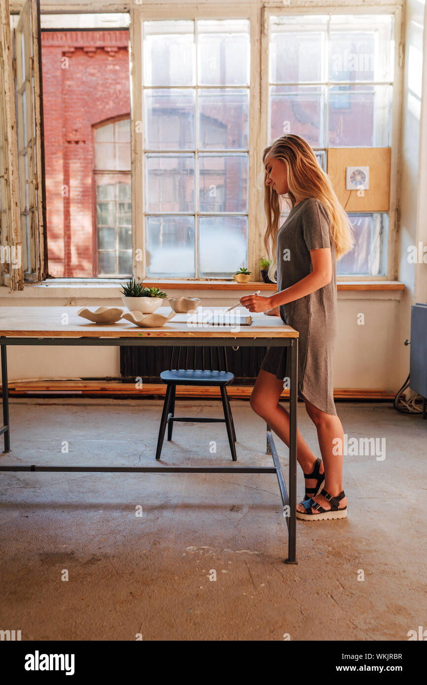 Female Ceramic Artist Thinking Over Sketches At Desk Side View Of