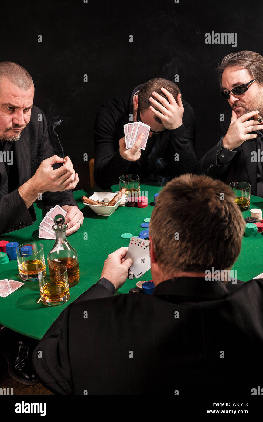 Photo of men playing poker, drinking and smoking, and looking uncertain of their luck. Stock Photo