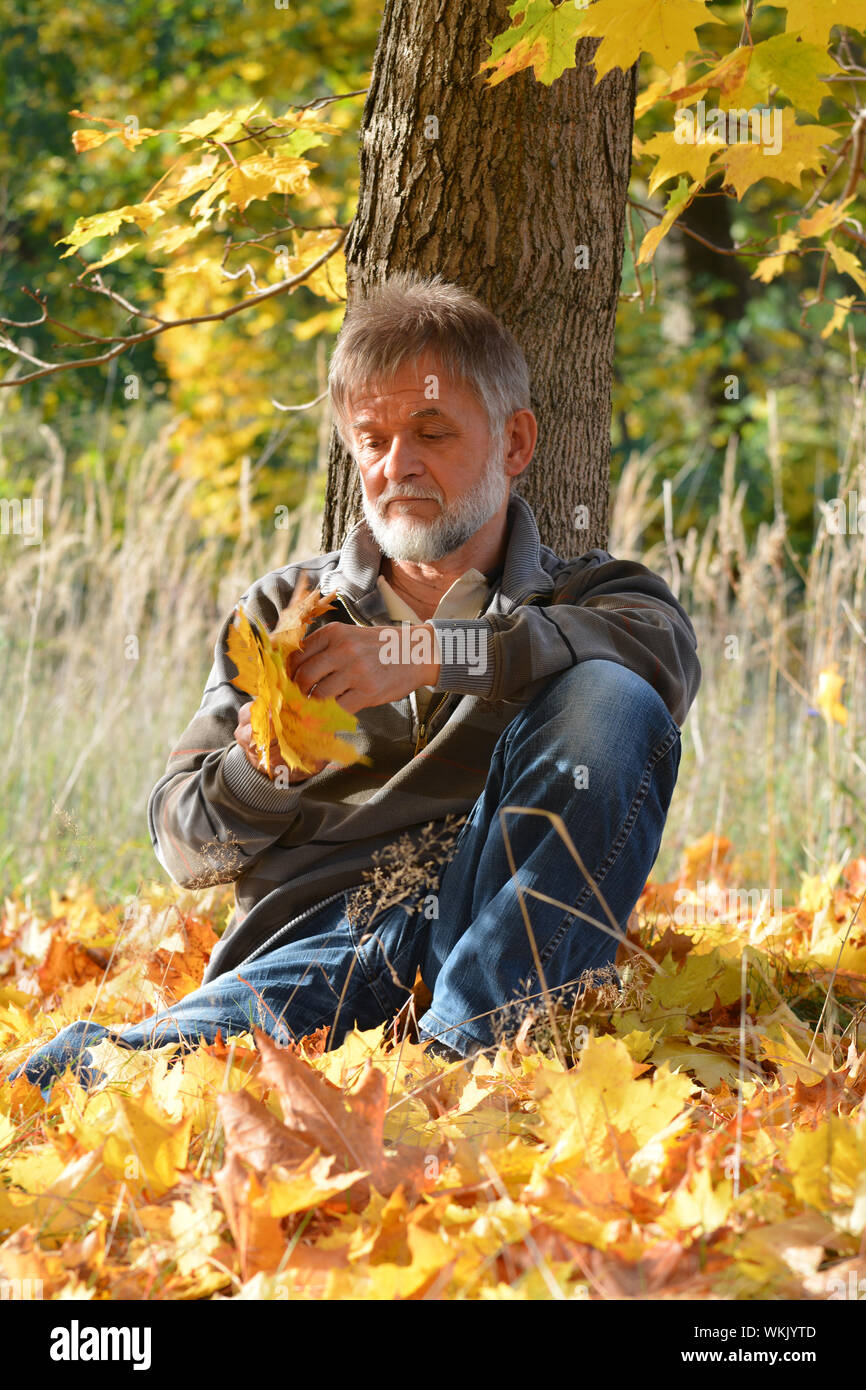 Old man sadly sits under a tree Stock Photo