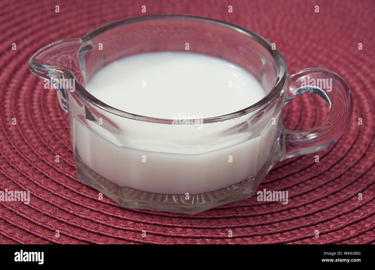 Pink depression glass creamer pitcher with cream in a closeup photo on a burgundy place mat.  This beverage is cream used for coffee. Stock Photo