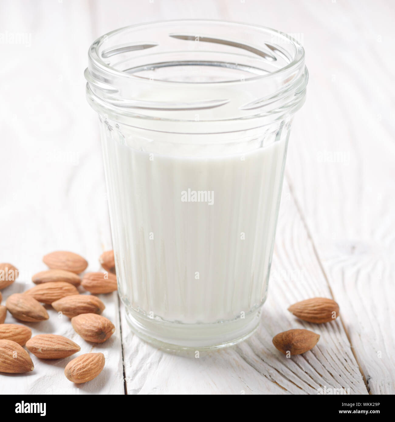 Milk or yogurt in mason jar on white wooden table with almonds aside