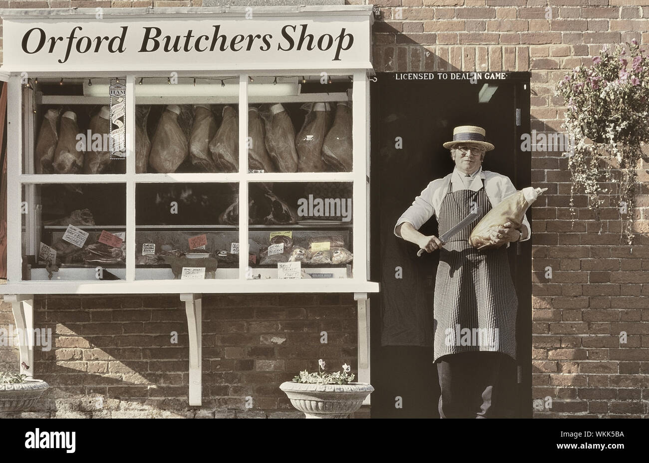 A traditional butcher proudly displays a cut of meat in the doorway of his local butchers shop. Orford. Woodbridge. Suffolk. England. UK Stock Photo