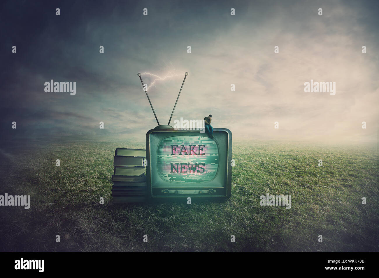 Surreal scene as a minuscule man seated on an old TV box in a open field, feeling disappointed of the fake news. Television manipulation and brainwash Stock Photo