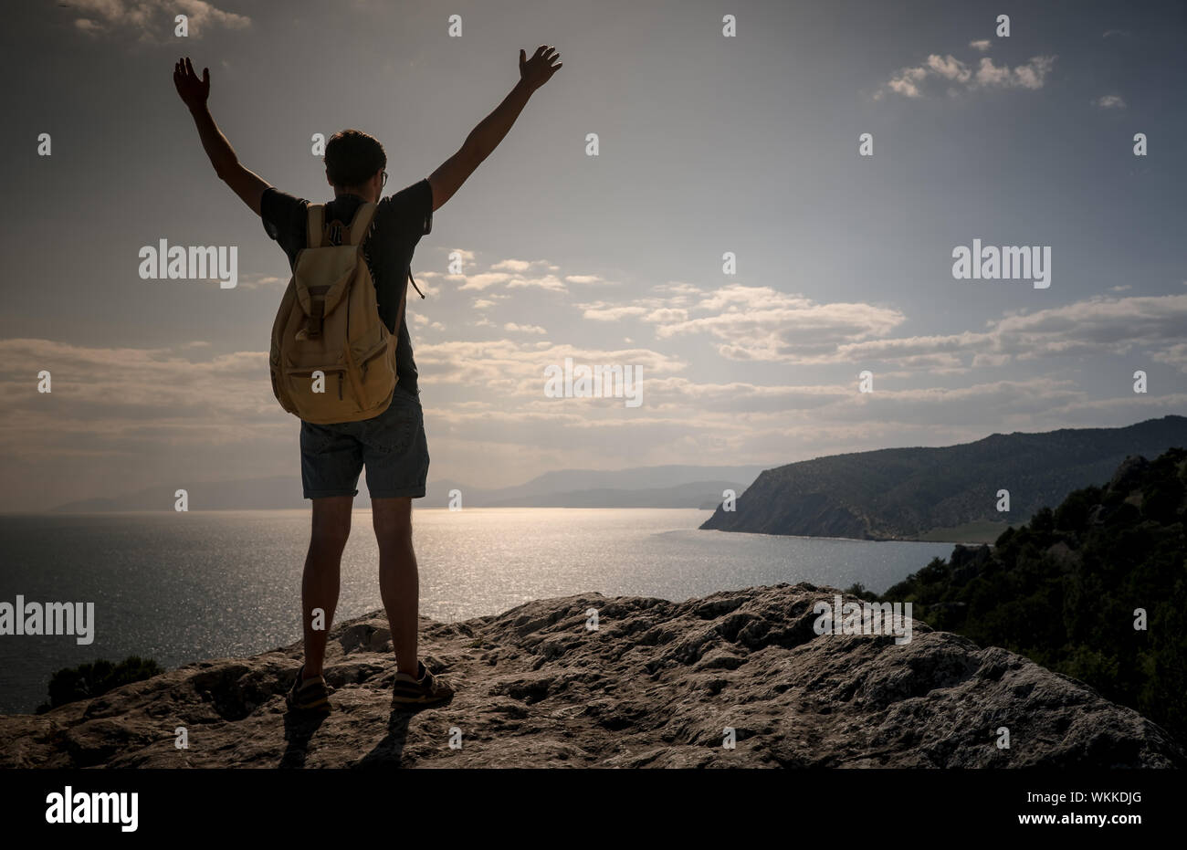 Hiker with backpack standing on top of a mountain with raised hands and ...