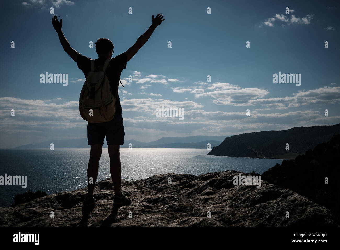 Hiker with backpack standing on top of a mountain with raised hands and ...