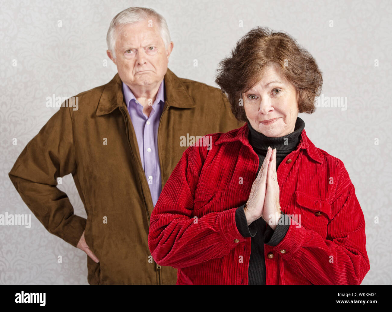 Coy pretty older woman in front of grumpy man Stock Photo