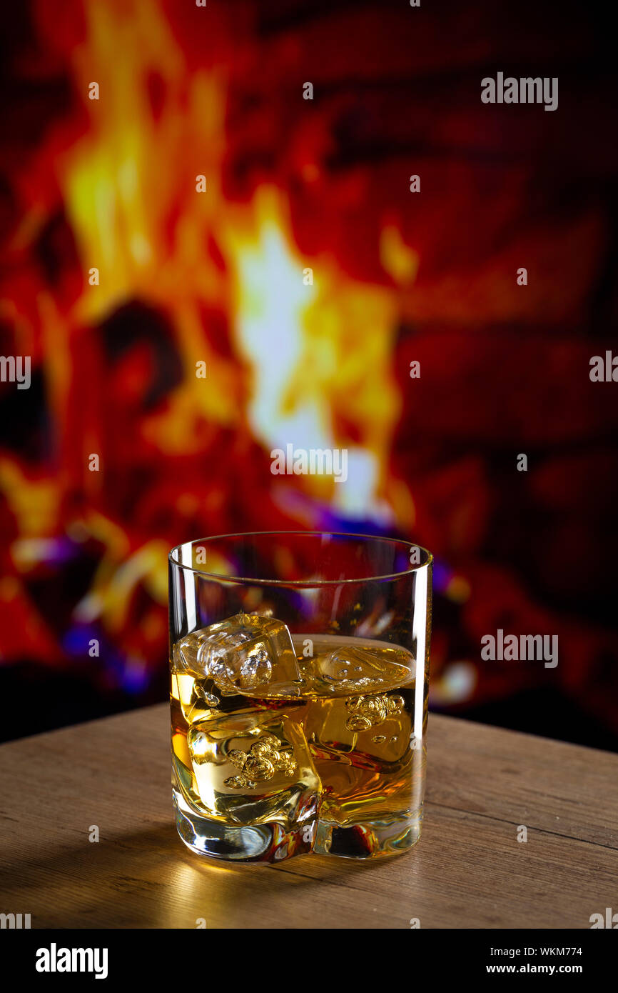 Glass Of Whiskey With Ice On A Wooden Table In Front Of A