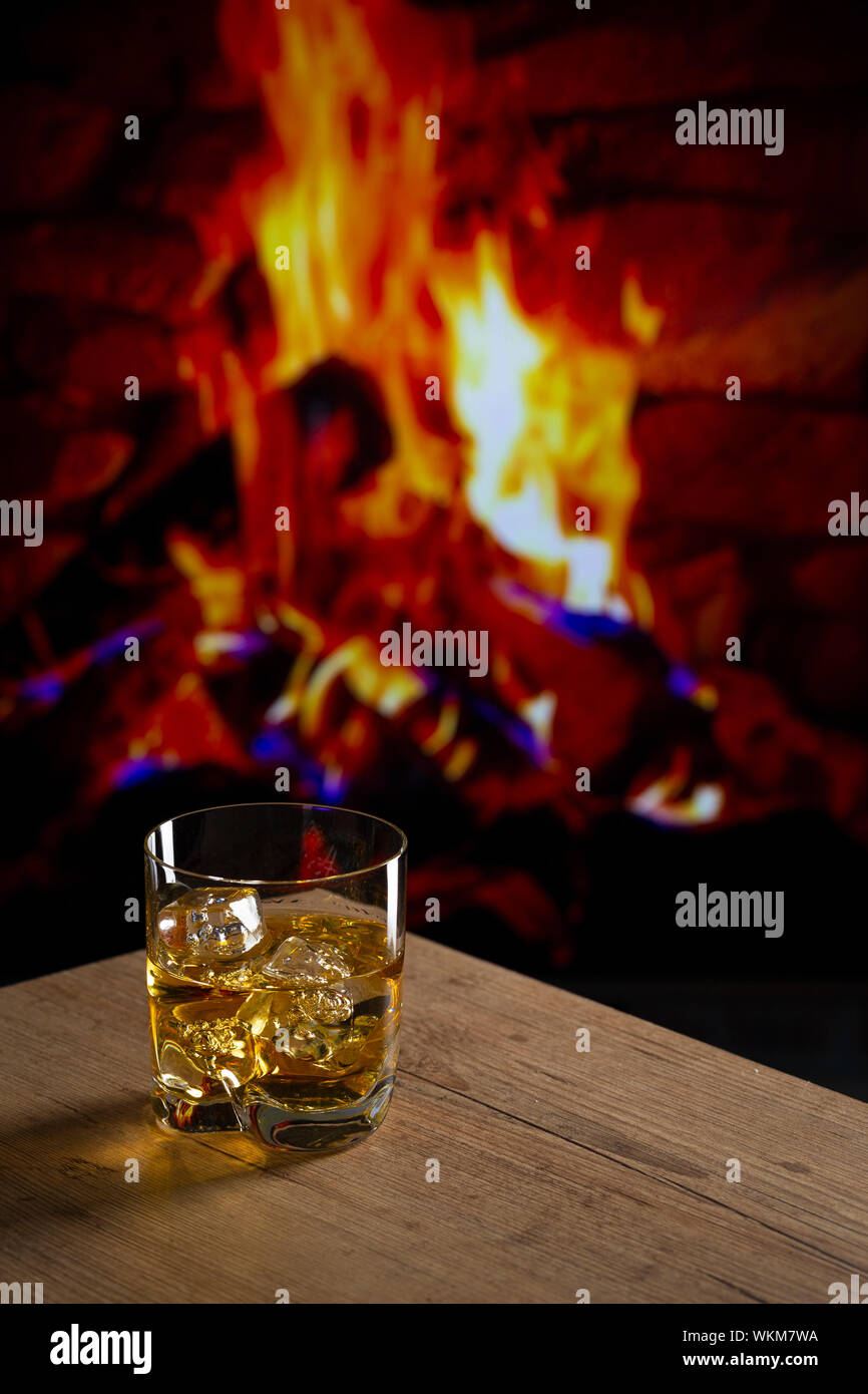 Glass Of Whiskey With Ice On A Wooden Table In Front Of A