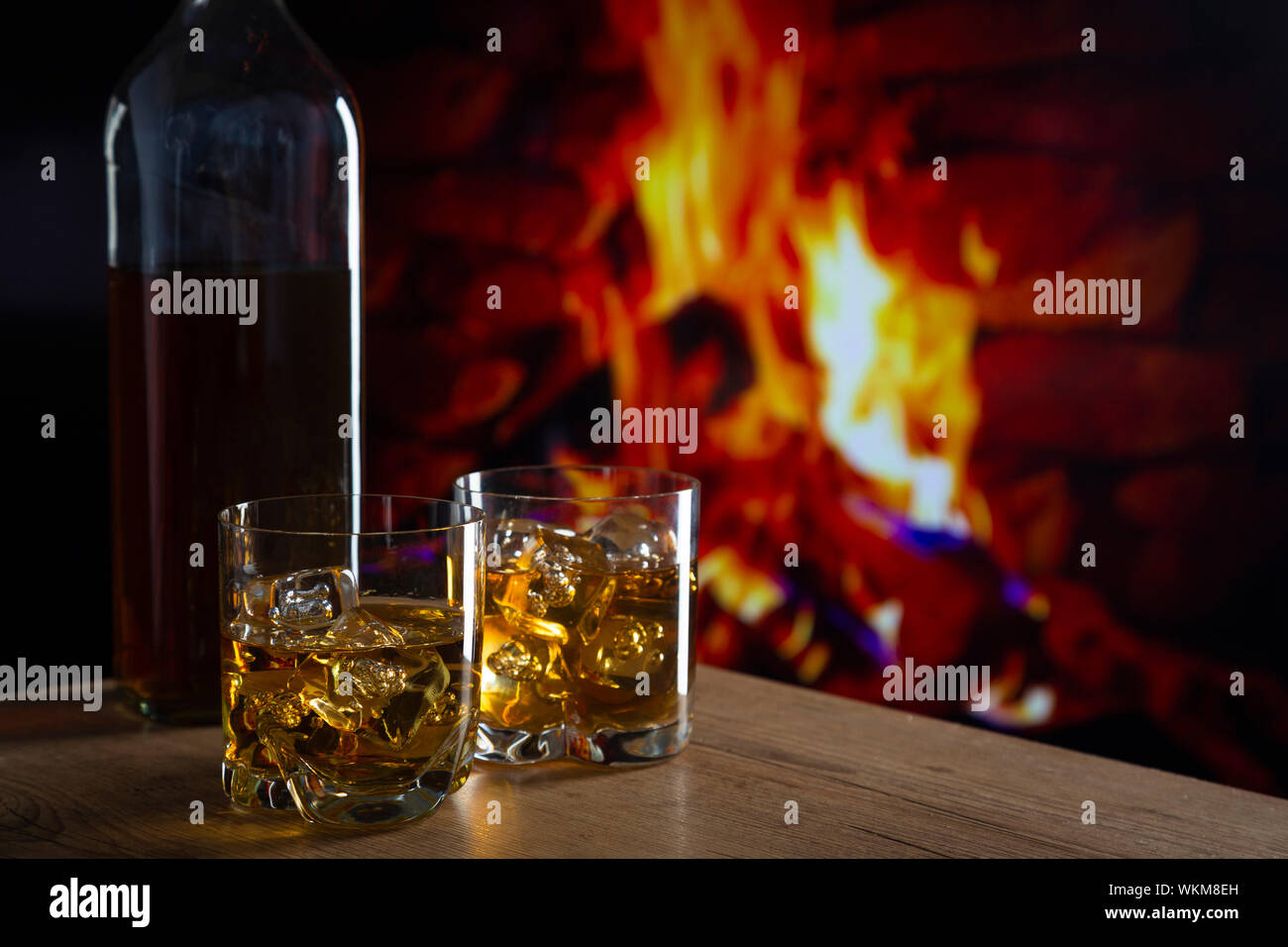 https://c8.alamy.com/comp/WKM8EH/glass-of-whiskey-with-ice-on-a-wooden-table-in-front-of-a-fireplace-WKM8EH.jpg