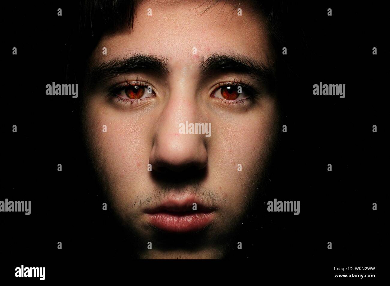 Close-up Portrait Of Man With Red Eyes Against Black Background Stock Photo