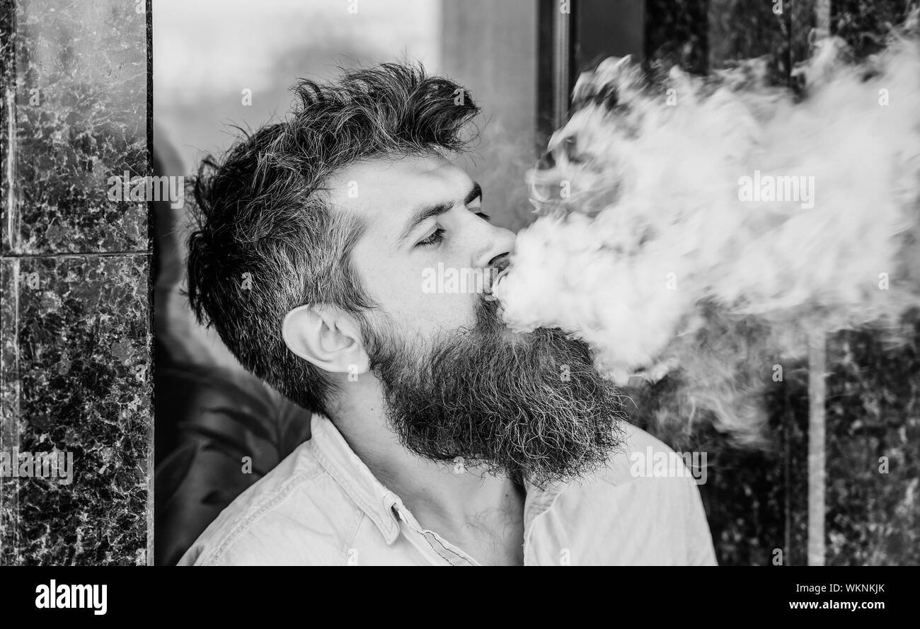 Smoking electronic cigarette. Stress relief concept. Smoking device. Man  long beard relaxed with smoking habit. Clouds of flavored smoke. Bearded  man smoking vape. Man with beard breathe out smoke Stock Photo -