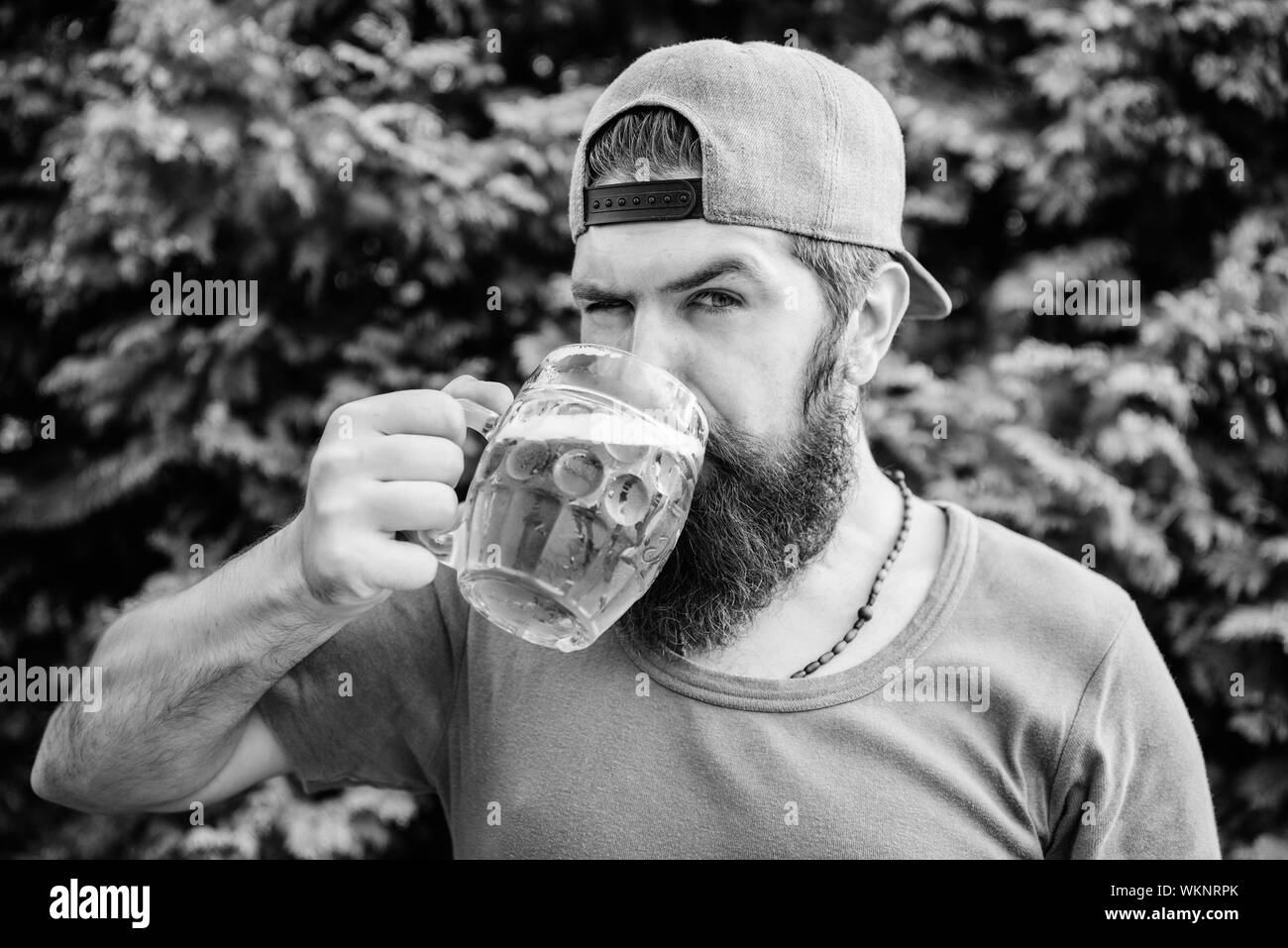 Enjoying his alcoholic beer. Bearded man drinking alcoholic drink in summer. Hipster with alcoholic beverage on nature. He is a beer drinker not an alcoholic. Stock Photo
