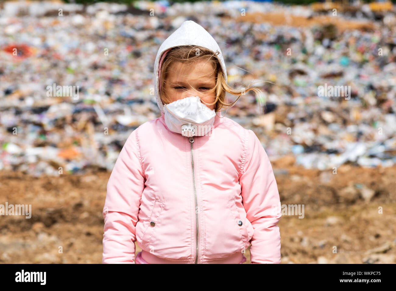 Little girl on the background of a municipal landfill in a gas mask