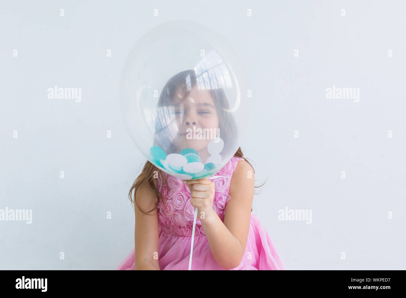 Smiling girl behind balloon.  Funny girl holding balloon in her  hand and hiding behind it - isolated over a white background Stock Photo