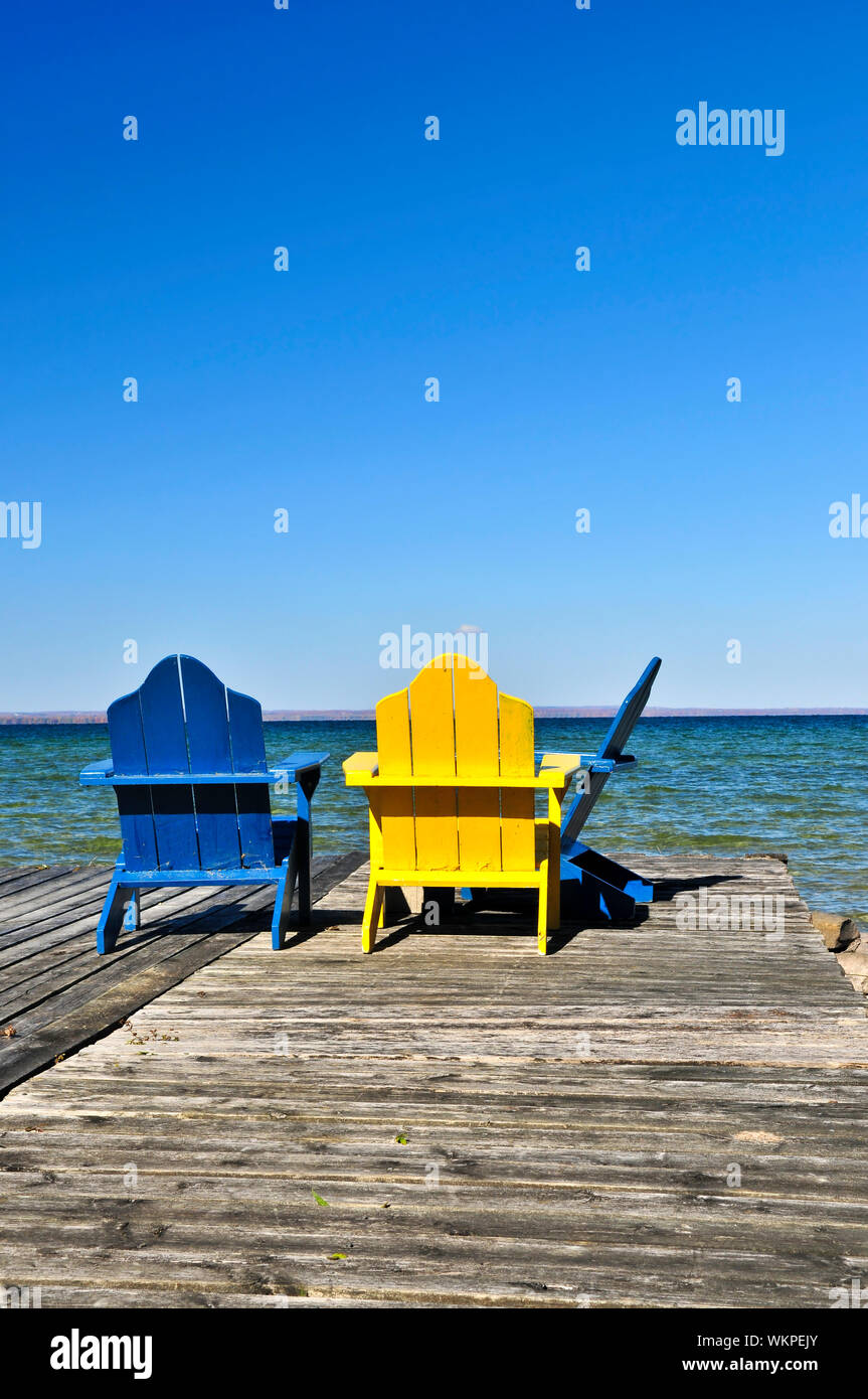 Painted wooden chairs on dock at a lake Stock Photo - Alamy
