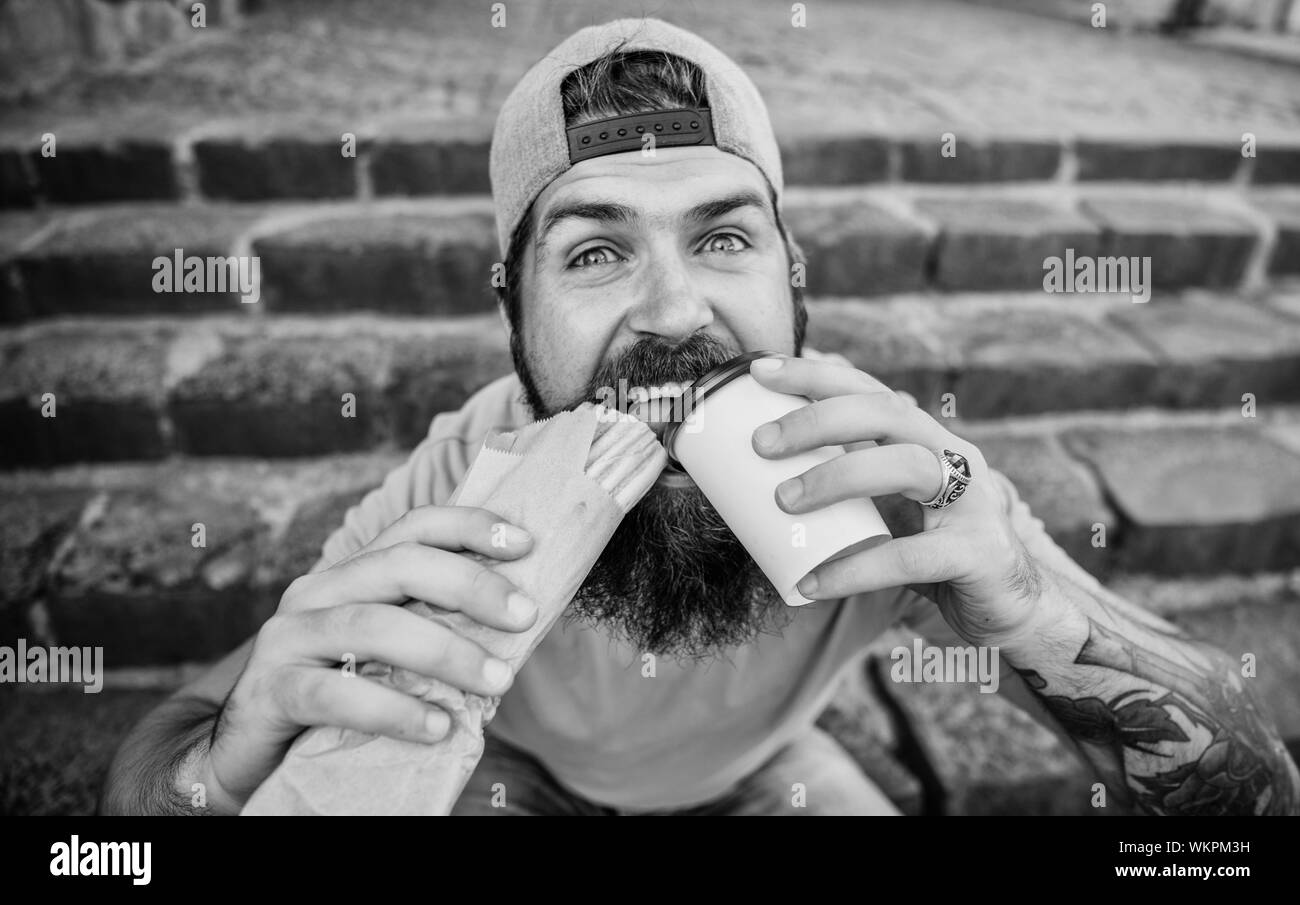 Unleashed appetite. Street food concept. Man bearded eat tasty sausage. Urban lifestyle nutrition. Junk food. Carefree hipster eat junk food while sit stairs. Guy eating hot dog. Snack for good mood. Stock Photo