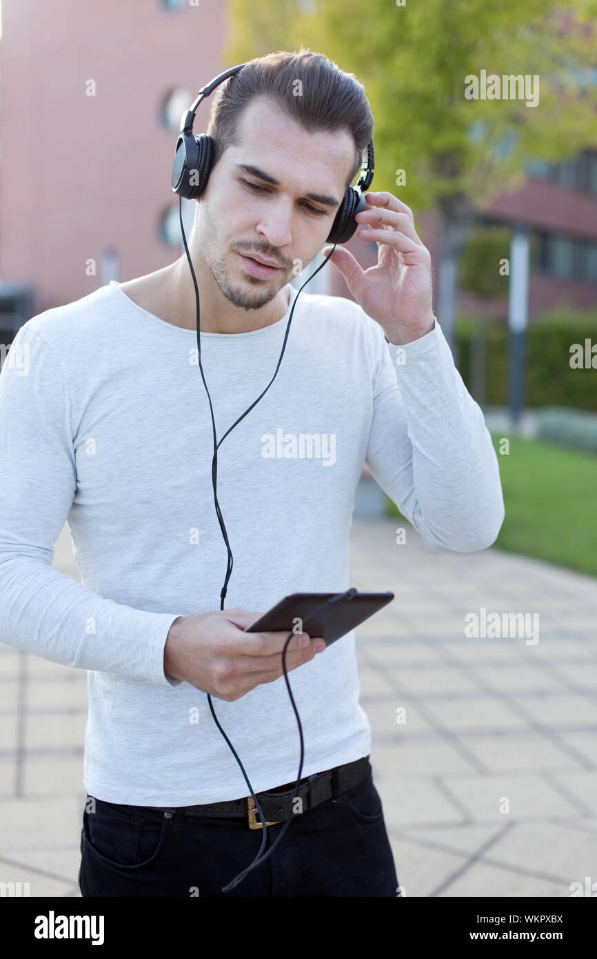 Young handsome guy listening music by headphones in park Stock Photo