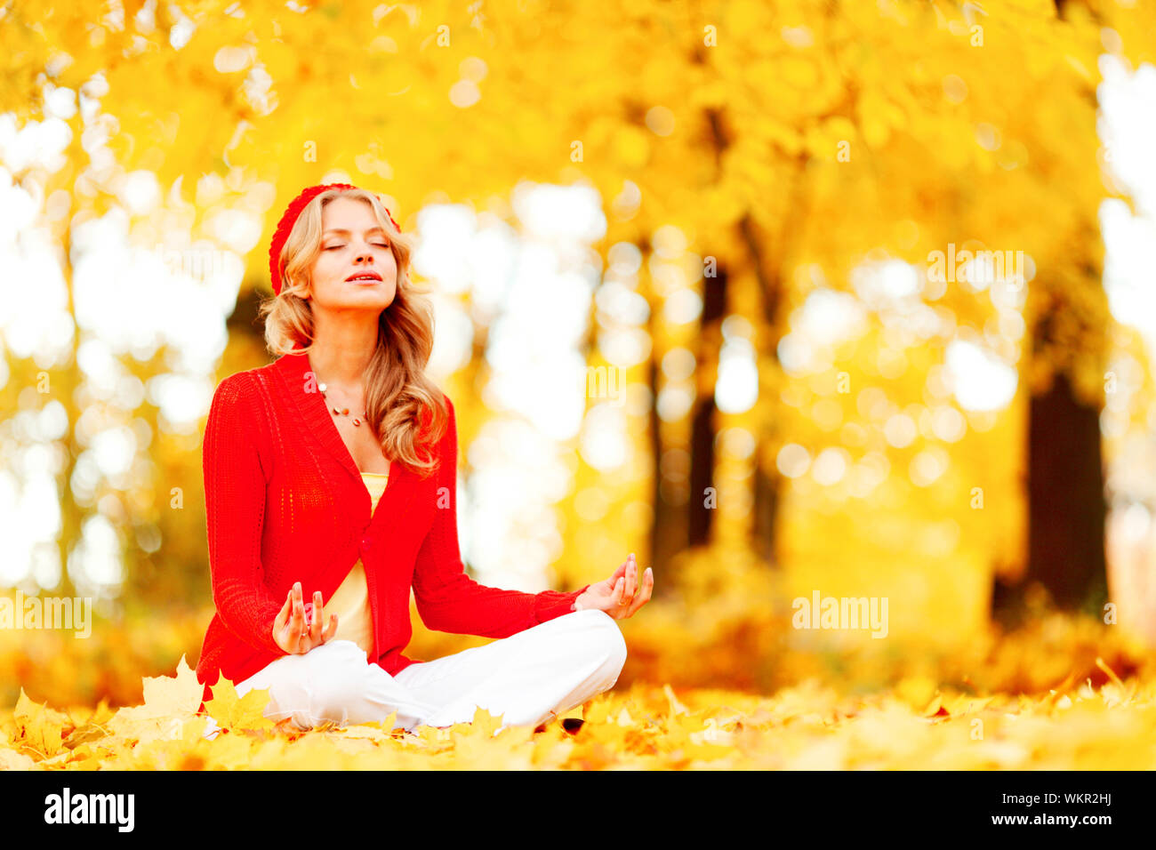 Beautiful young woman sitting in autumn park in lotus yoga position ...