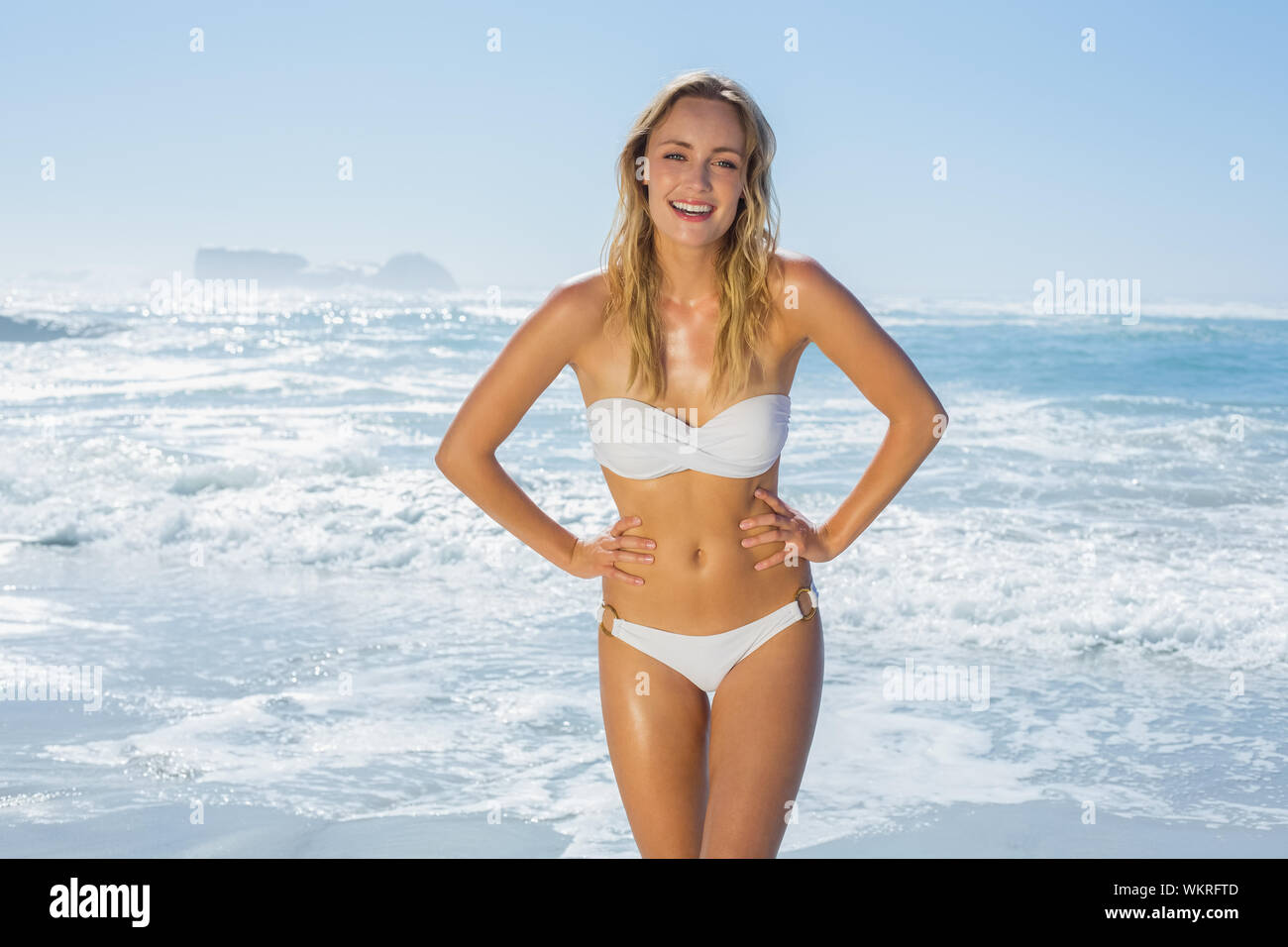 Gorgeous blonde in white bikini standing by the sea on a sunny day Stock Photo
