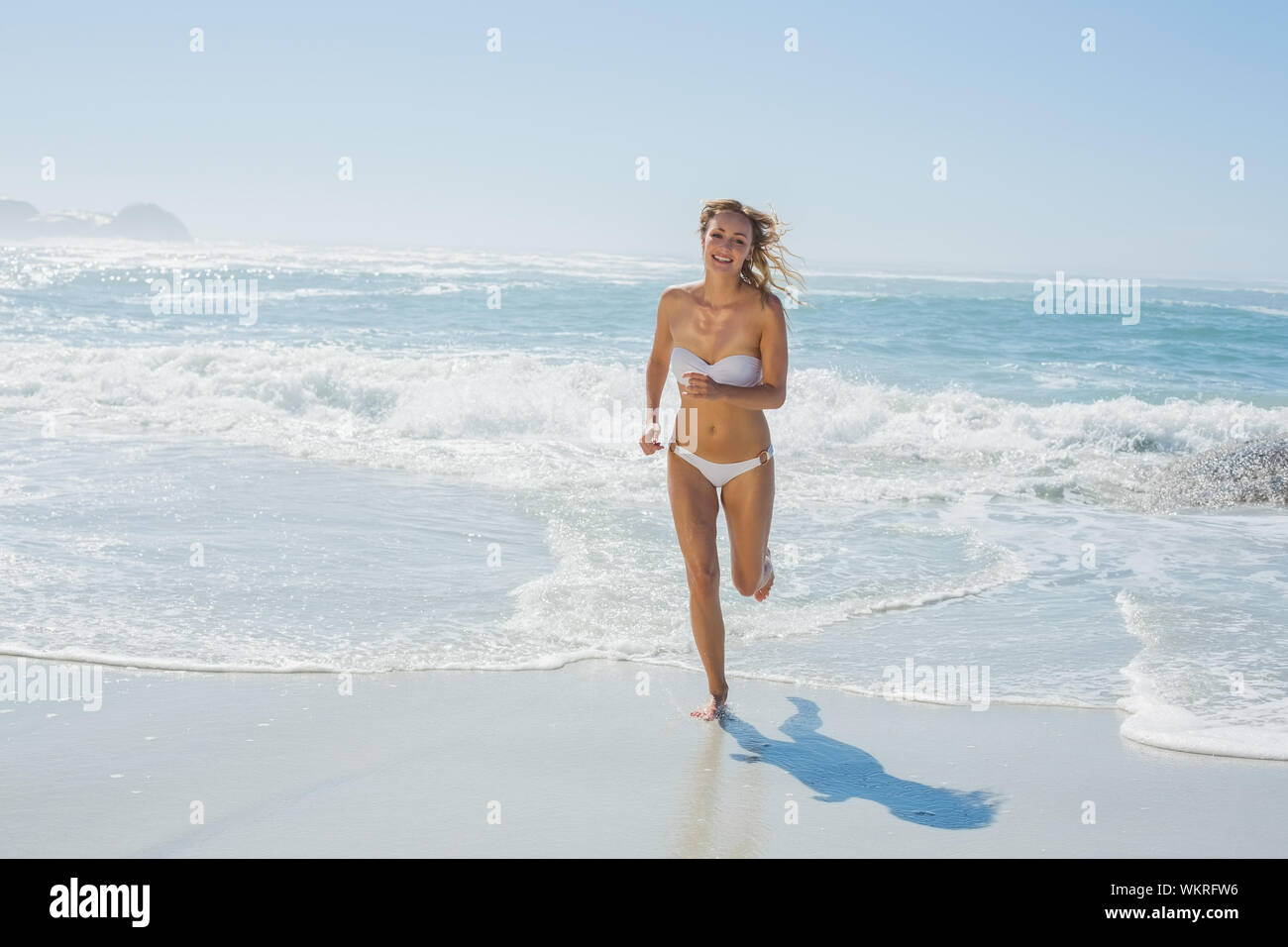 Gorgeous blonde in white bikini running from the sea on a sunny day Stock Photo