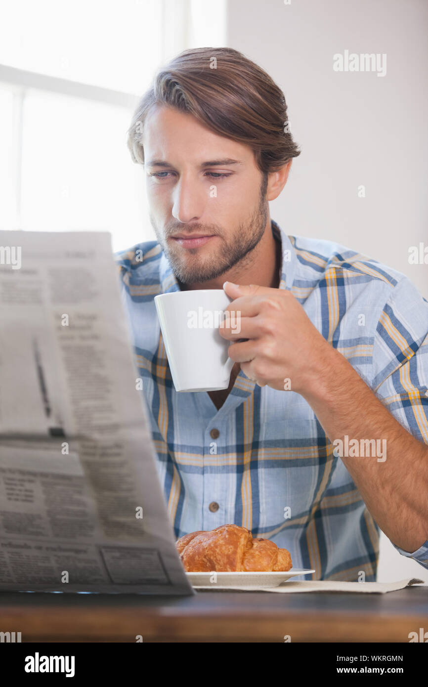 Handsome man drinking coffee and reading newspaper at home in the ...