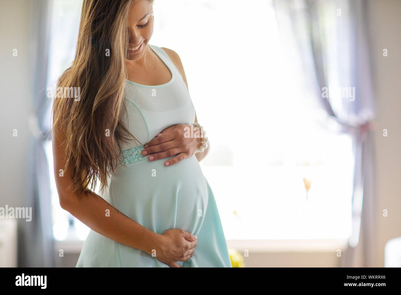 Smiling pregnant woman in dress with her hands at belly Stock Photo