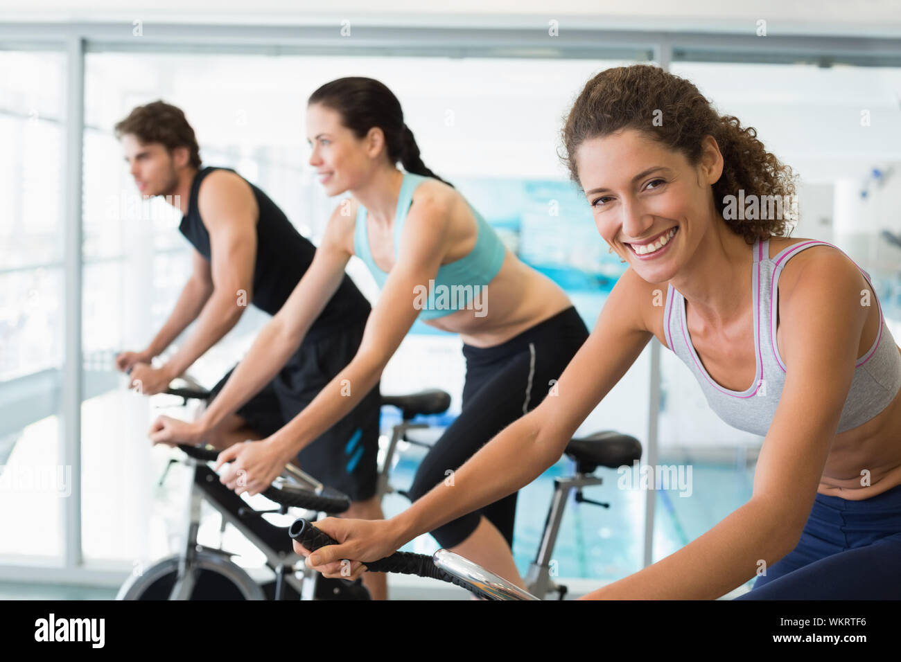 Fit people in a spin class with woman smiling at camera at the gym ...