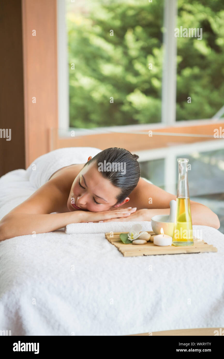 Brunette lying on massage table with tray of beauty treatments at the ...