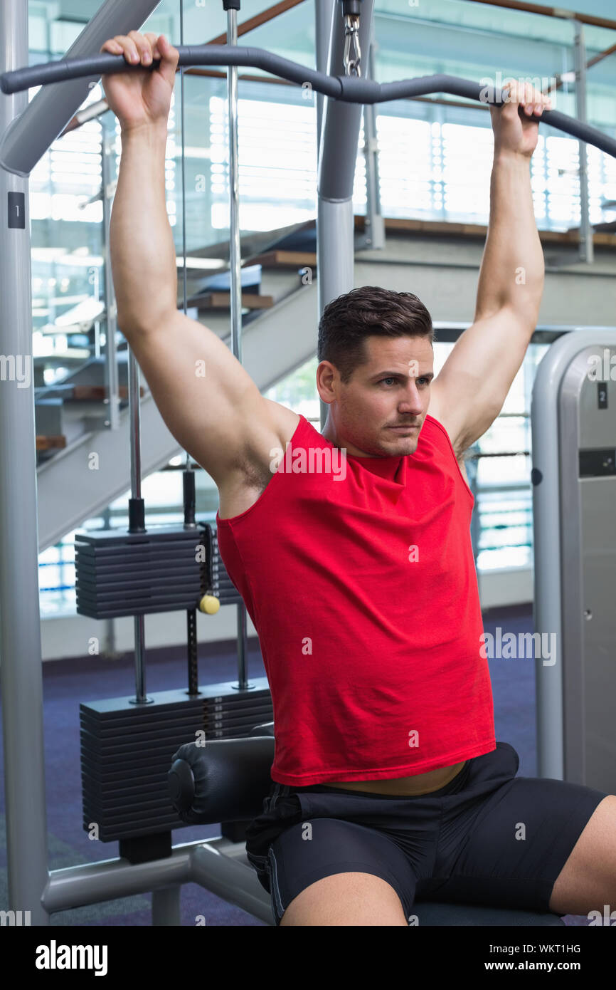 Handsome bodybuilder using weight machine for arms at the gymer