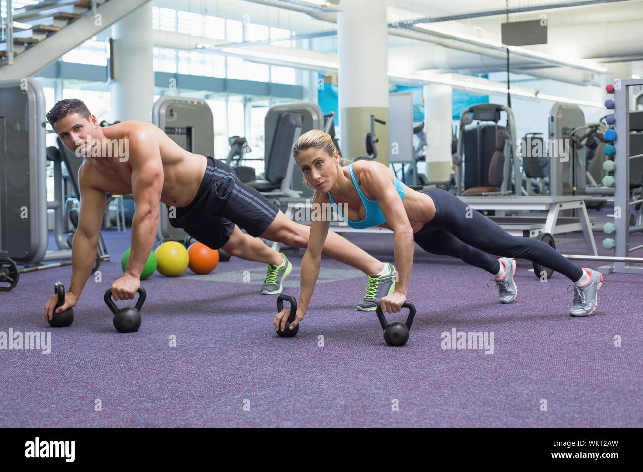 Bodybuilding man and woman lifting kettlebells in plank position at the