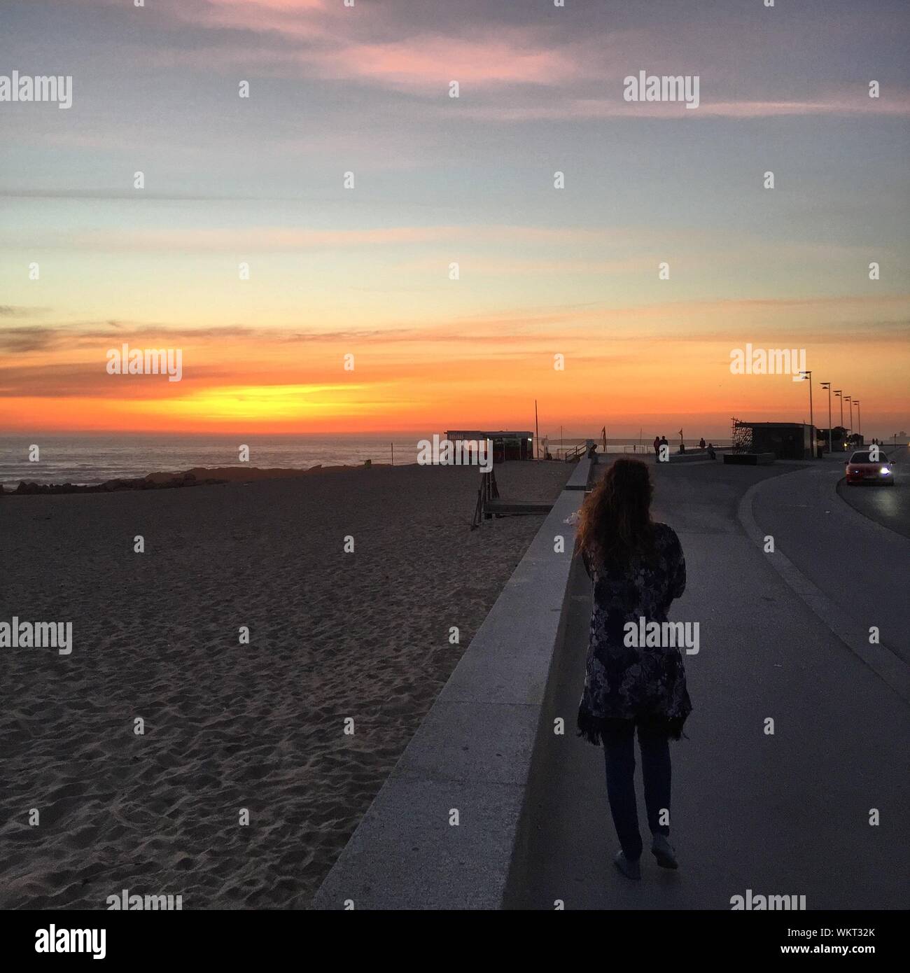 Full Length Rear View Of Woman Beach Against Orange Sky Stock Photo