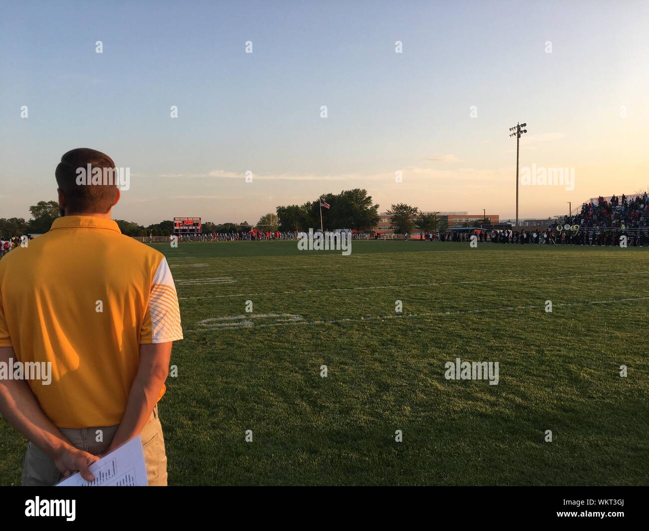 Rear View Of Man Standing On Sports Field Against Sky During Sunset Stock Photo