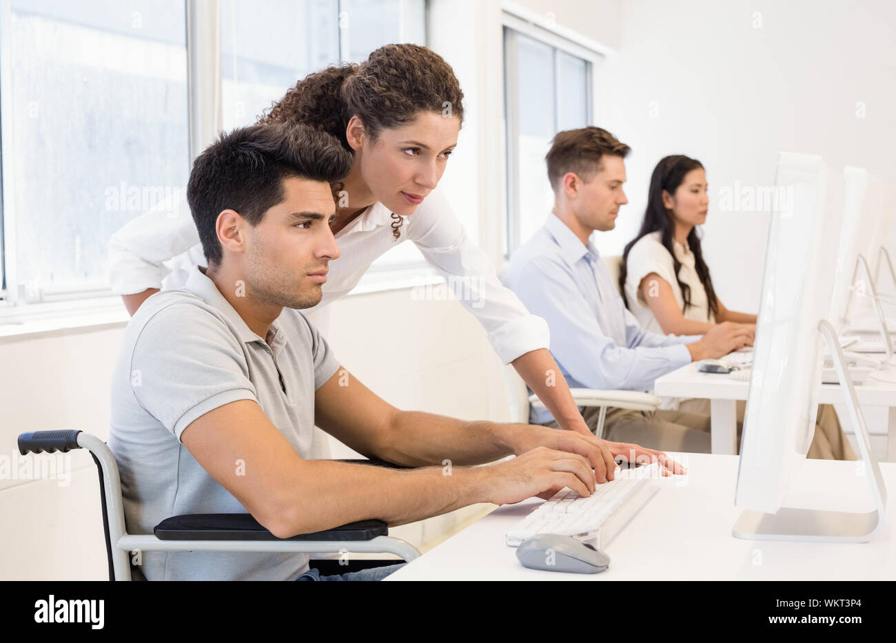 Casual businesswoman helping colleague in wheelchair in the office Stock Photo