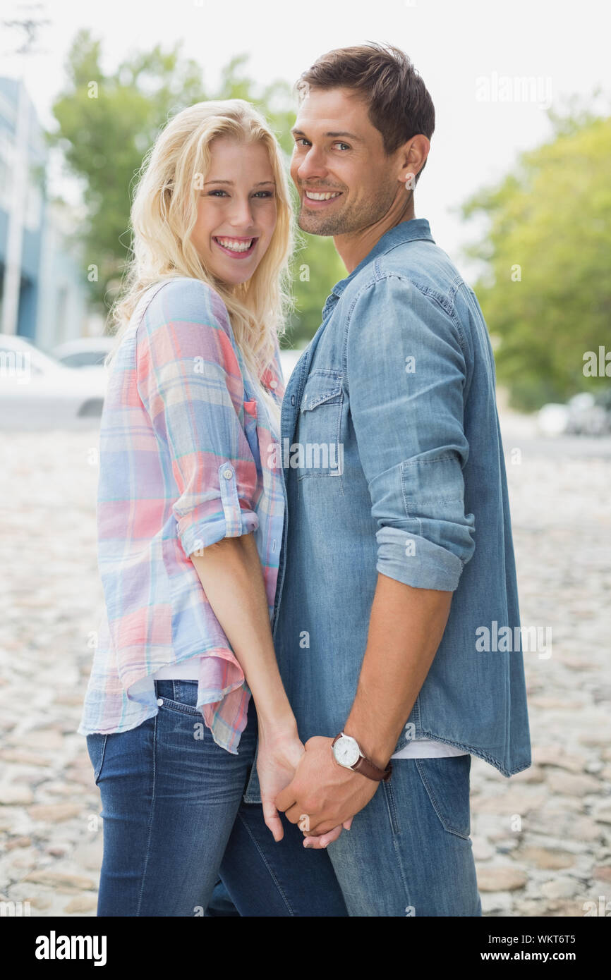 Hip young couple holding hands smiling at camera on a sunny day in the ...