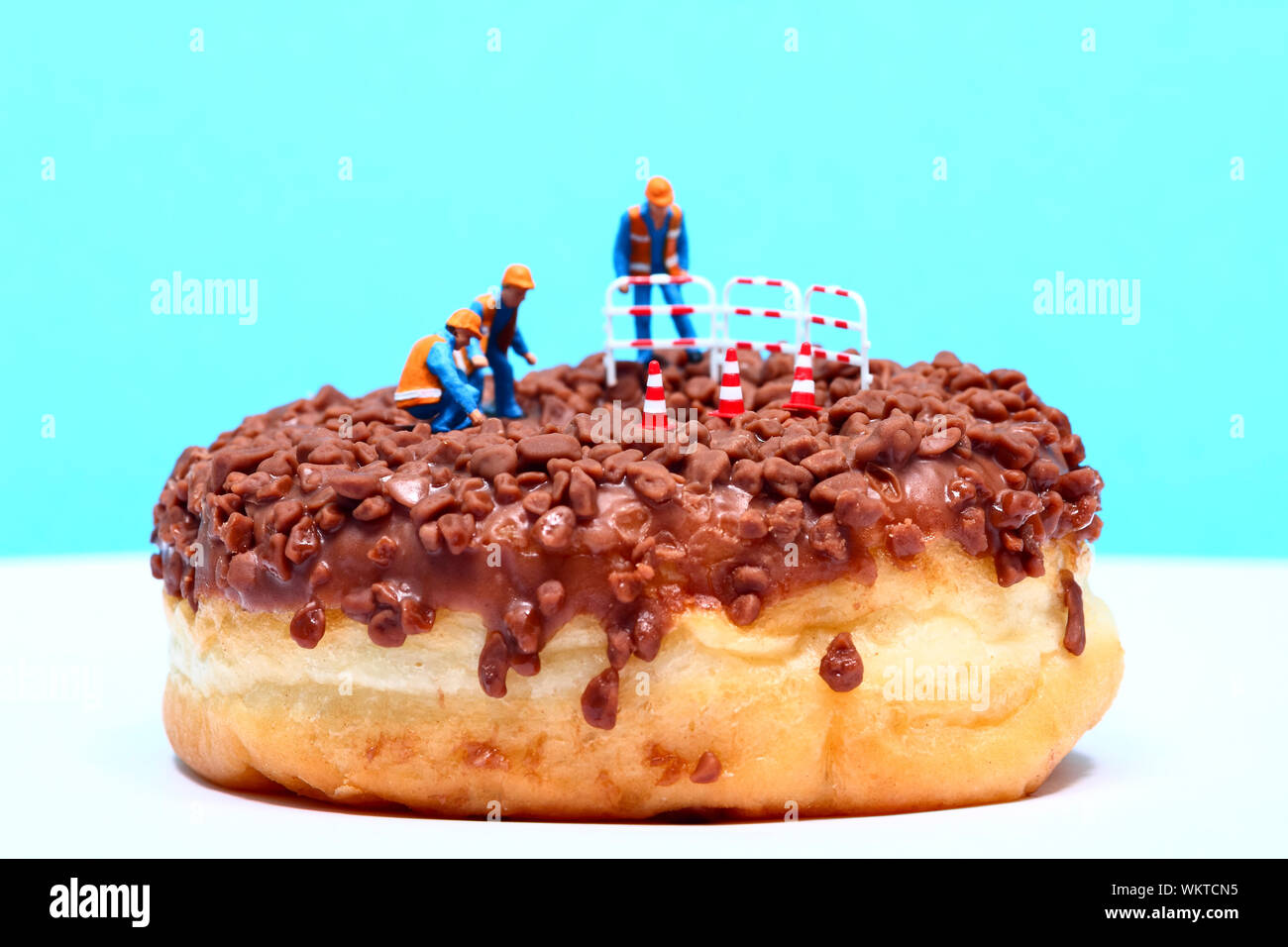 Conceptual image of a miniature figure workmen stood on a chocolate doughnut looking down the centre hole Stock Photo