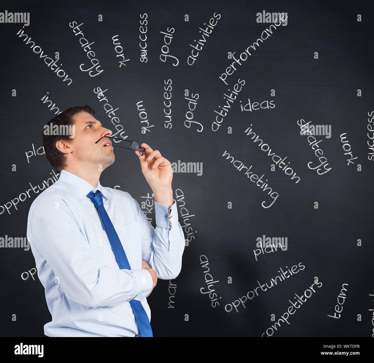 Thinking businessman biting glasses against blackboard with business buzzwords Stock Photo