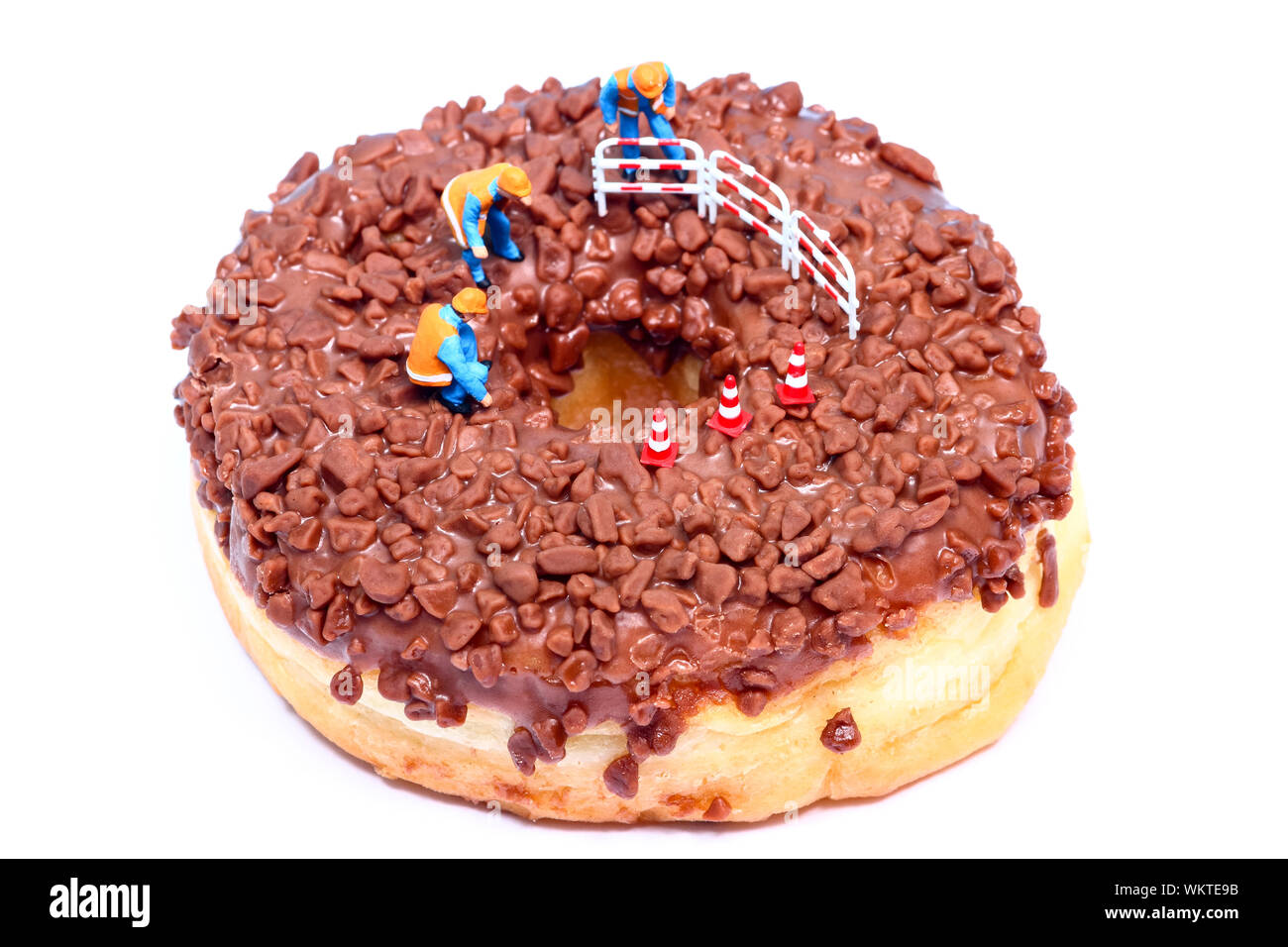 Conceptual image of a miniature figure workmen stood on a chocolate doughnut looking down the centre hole Stock Photo