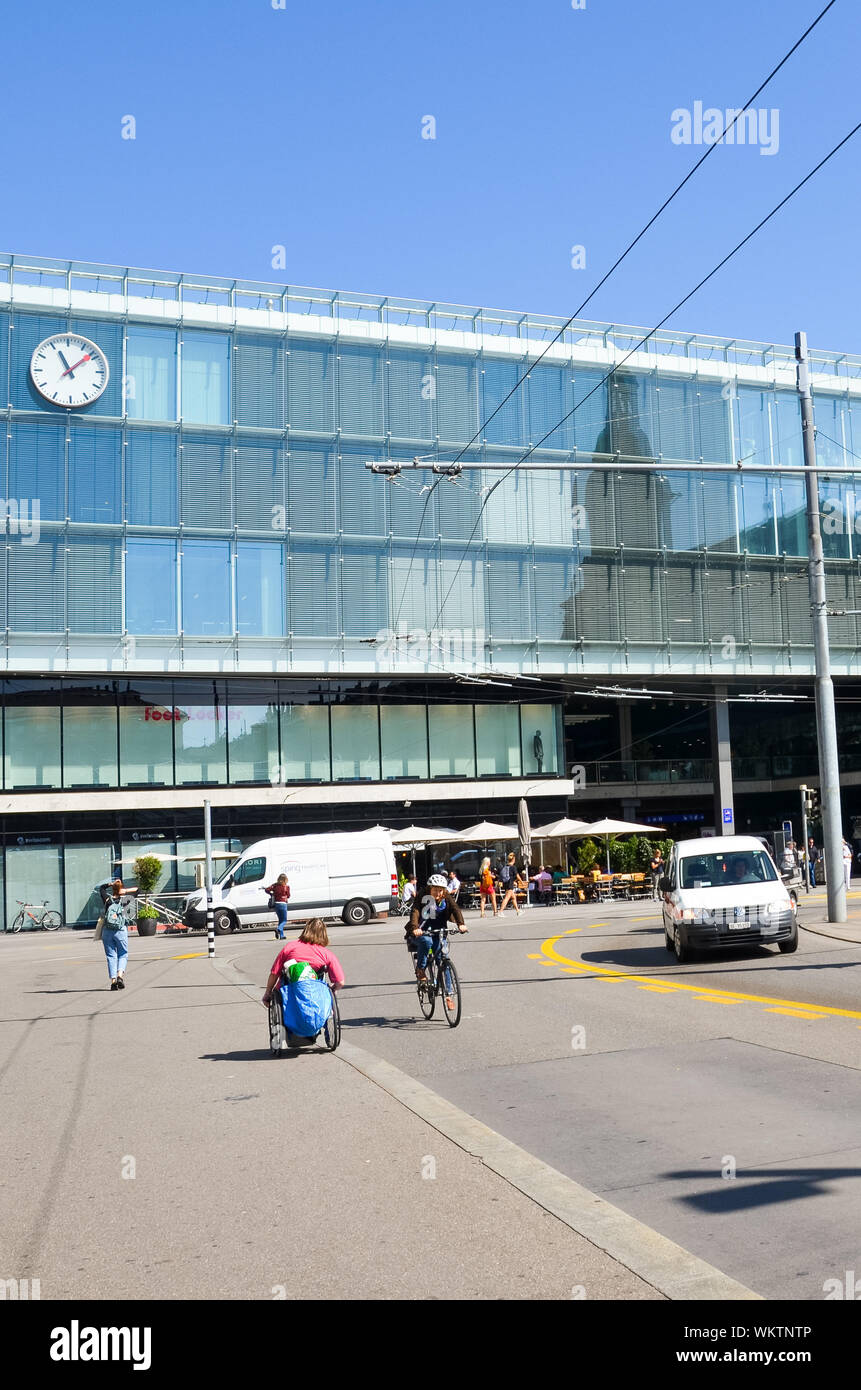 Bern, Switzerland - August 14, 2019: Building of the main train station in Swiss capital photographed from outside with people on the street and cars on the adjacent road. Vertical picture. Stock Photo