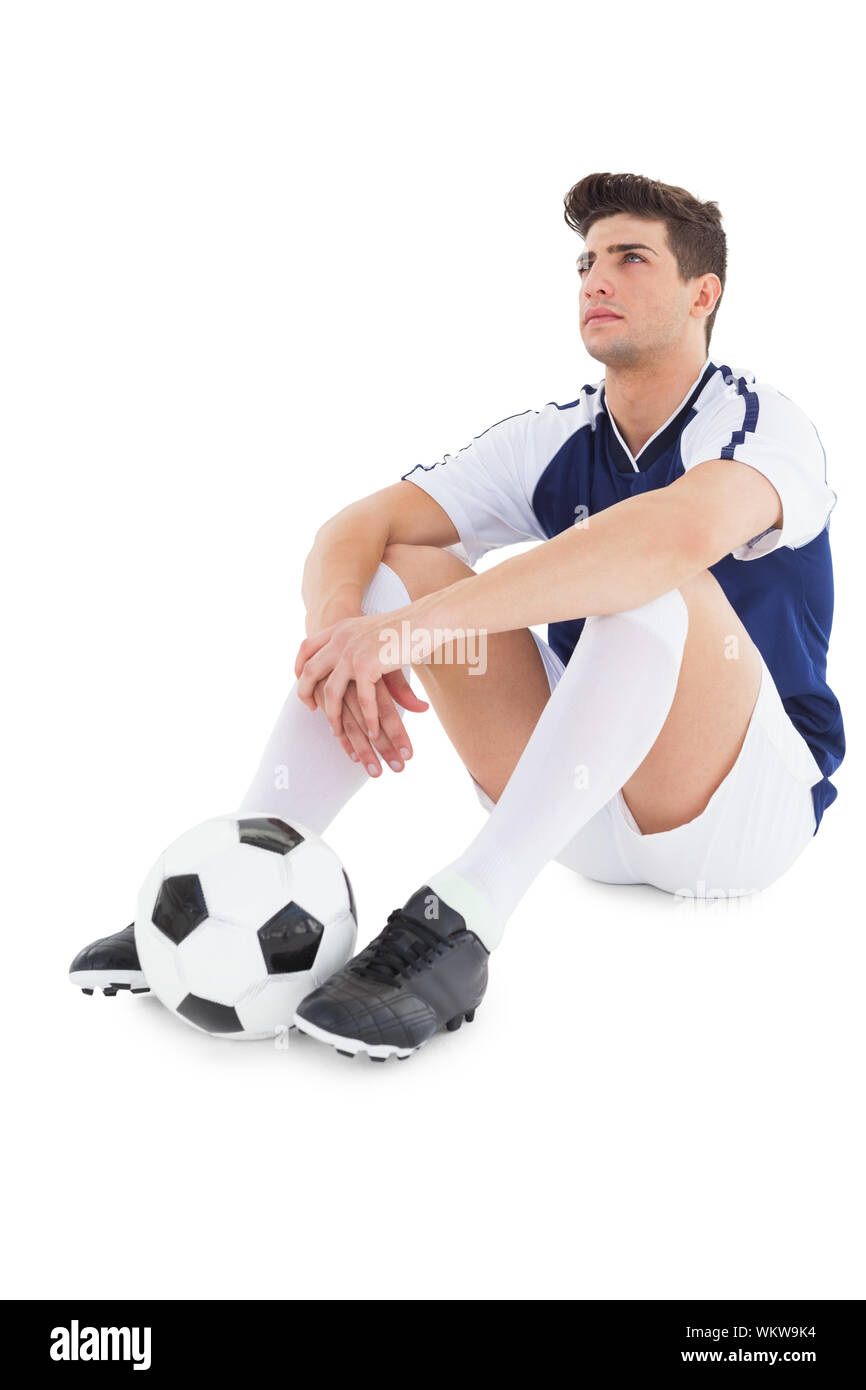 Football player sitting on the ground with ball on white background