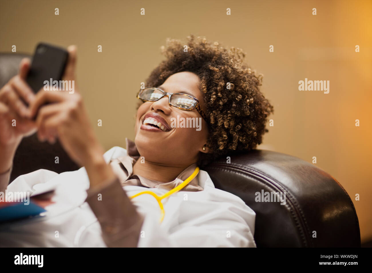 Female doctor taking a break, and text messaging on a sofa. Stock Photo