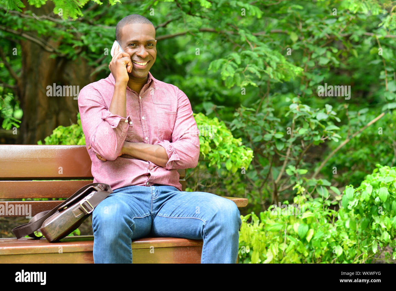 Casual man sitting on park bench and talking on cell phone Stock Photo